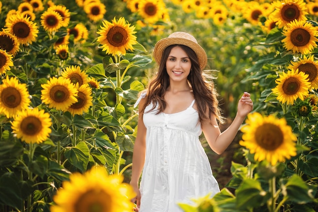 Sweet woman in a white dress walking on a field of sunflowers