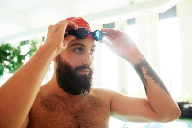 A swimmer in a cap and goggles puts on swimming goggles smiling before swimming training in the pool