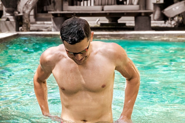 Swimmer portrait of smiling athletic man with bare torso wearing glasses for swimming in pool concep