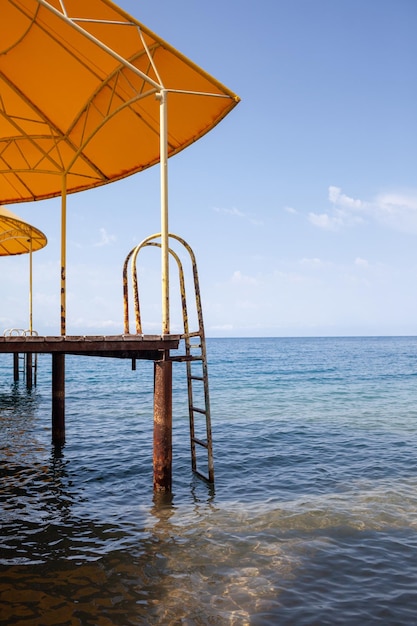 Swimming area or pier on the sea A large pier with a roof, wooden planks and rusty stairs descending