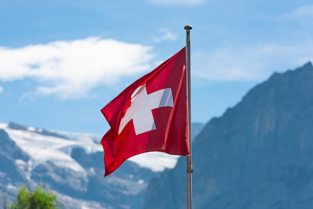 Swiss flag against Alps mountains. Horizontal shot with a selective focus