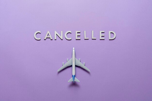 A symbol of cancelled airplane flight, word "cancelled" with plane flat lay on color surface