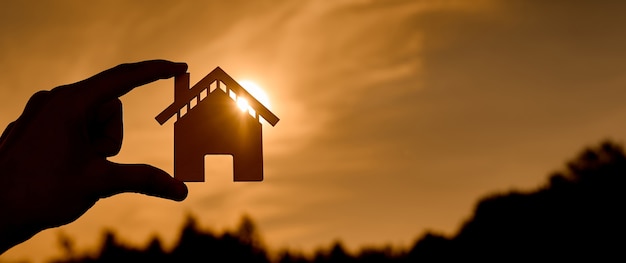 Symbol of the house at sunset in the form of contours in women's hands. High quality photo