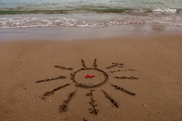 Symbol of the sun and a plane by the sea painted sun on the sand sea coast figure of a red plane sea...