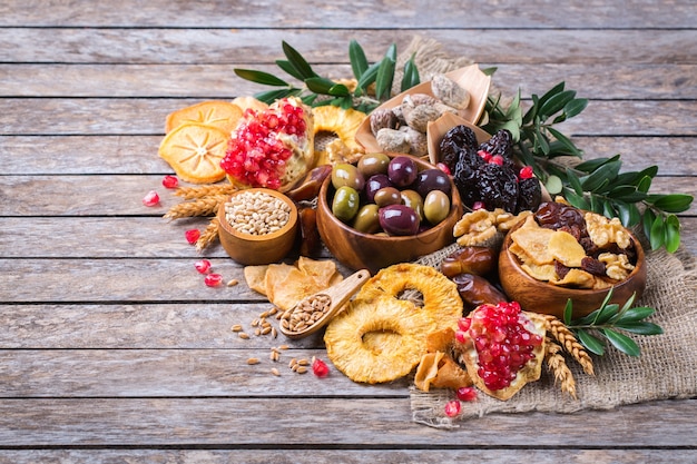 Symbols of judaic holiday Tu Bishvat, Rosh Hashana new year of the trees. Mix of dried fruits, date, fig, grape, barley, wheat, olive, pomegranate on a wooden table. Copy space background