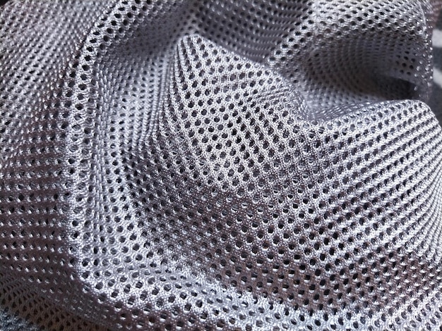 Synthetic polyester fabric with holes Abstract background A wavefolded piece of fabric in gray or silver color