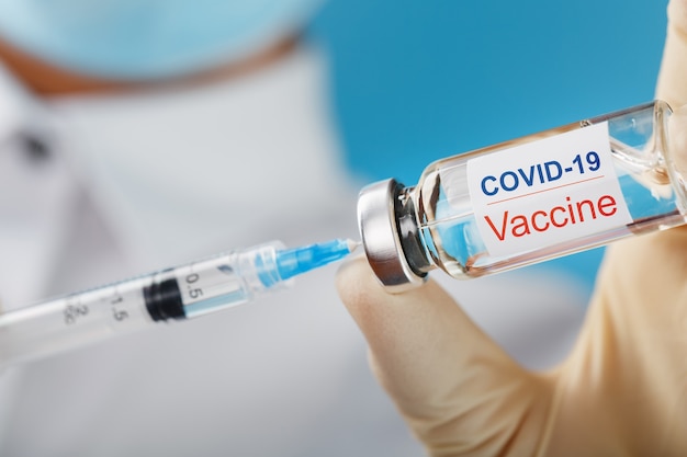 Syringe and ampoule with the inscription COVID-19 vaccine in the hands of a doctor-researcher