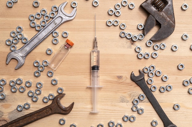 Syringe filled with liquid bottle of vaccine lies on table among variety of wrenches and metal nuts