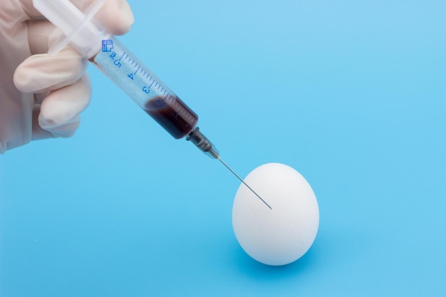 The syringe is injected into the egg closeup on a blue background The topic of vaccination of pregnant women