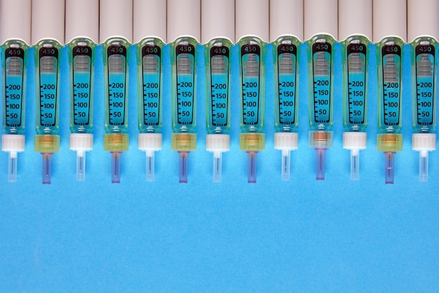 Syringe pens with insulin lined up in a row on a blue background Top view with copy space Flat lay