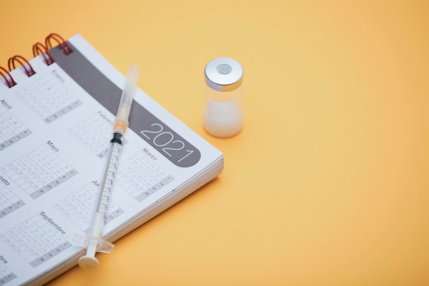 Photo syringe and vaccine canister, with calendar 2021, yellow background