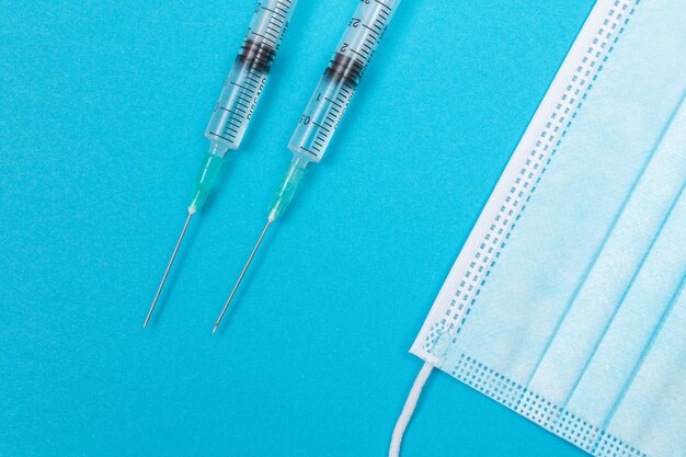 Syringe with medical mask on blue table  flat lay