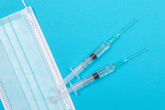 Syringe with medical mask on blue table  flat lay