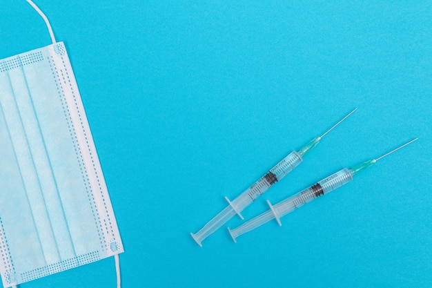 Syringe with medical mask on blue table  flat lay