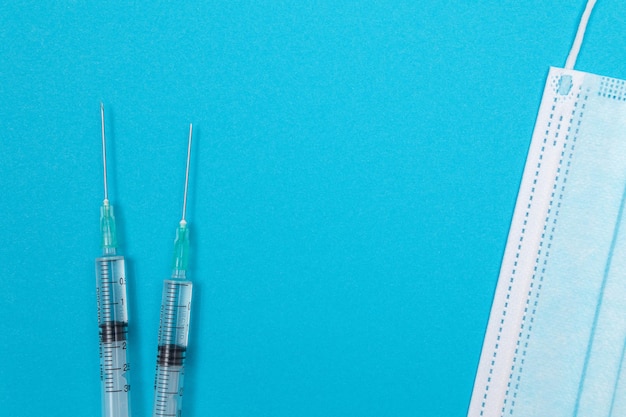 Syringe with medical mask on blue table  flat lay