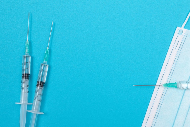 Syringe with medical mask on blue table flat lay