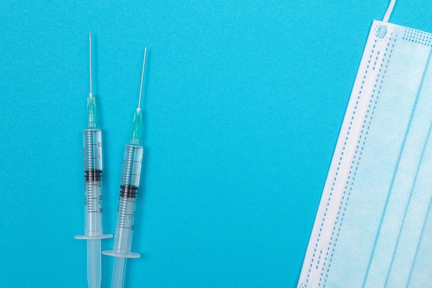 Syringe with Medical Mask on Blue Table Flat Lay