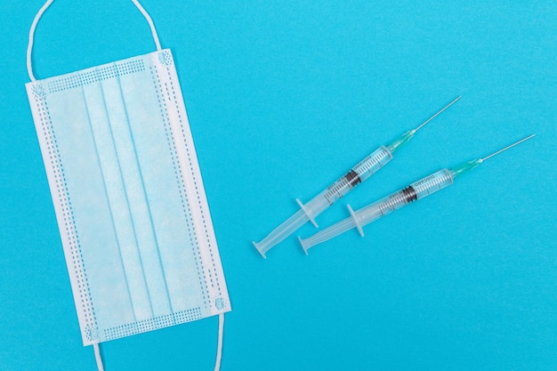 Syringe with Medical Mask on Blue Table Flat Lay