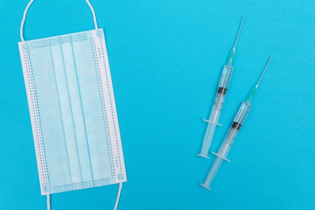 Syringe with medical mask on blue table  flat lay