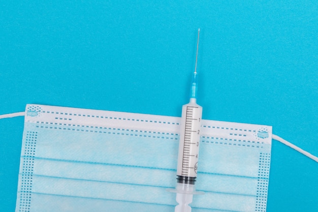 Syringe with medical mask on blue table  flat lay