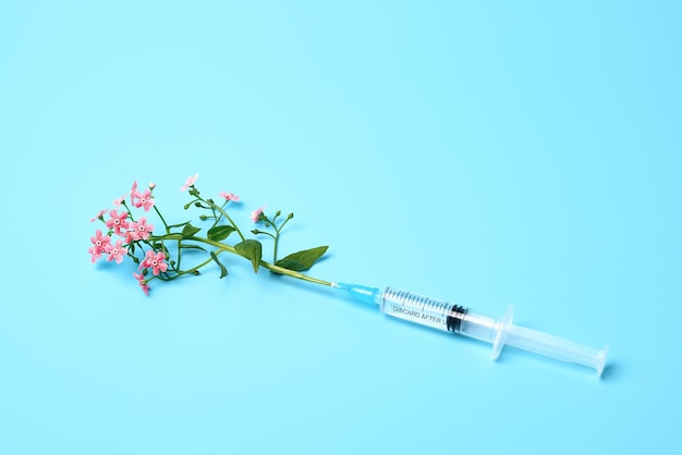 Syringe with pink flowers on blue background beauty injections creative concept