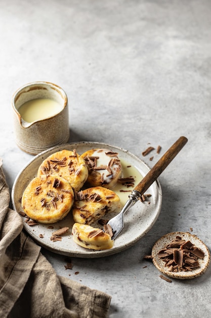 Syrniki or cottage cheese fritters with chocolate poured with condensed milk in the process of eating on ceramics plate with text space