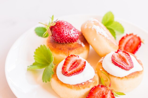 Syrniki, curd or cottage cheese pancakes withstrawberry, powdered suga on a white table.