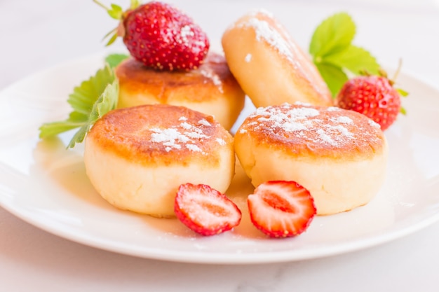 Syrniki, curd or cottage cheese pancakes withstrawberry, powdered suga on a white table.