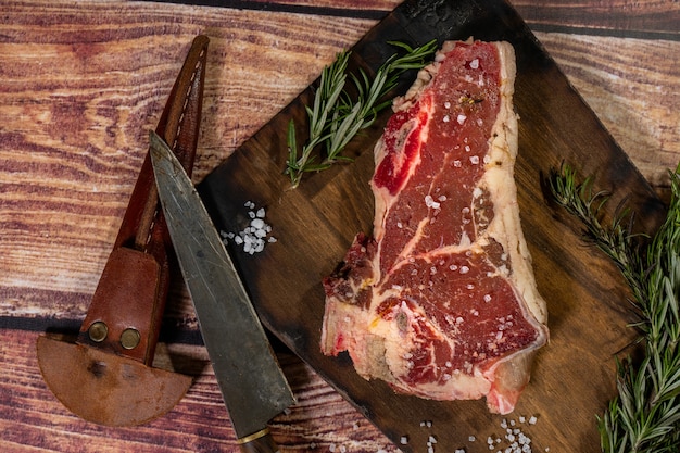 T-bone steak on a rustic wooden cutting board with herbs. Top view.