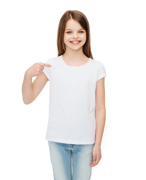 t-shirt design concept - smiling little girl in blank white t-shirt pointing at herself