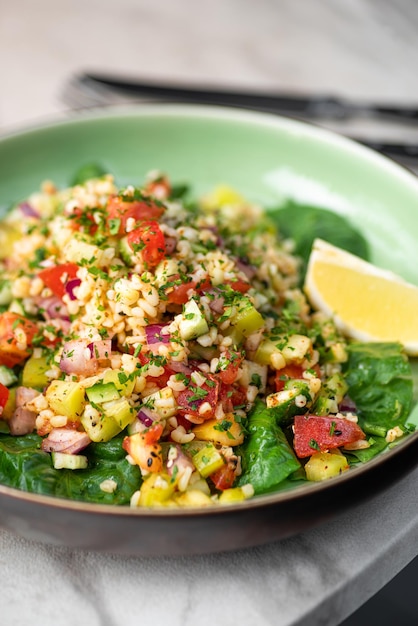 Tabbouleh salad with bulgur tomatoes parsley green onion and mint in plate on grey stone table Traditional middle eastern or arab dish