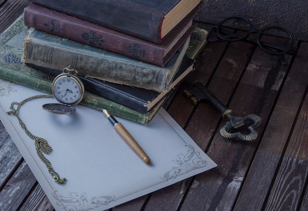 on the table are old books, pocket watches, fountain pen, glasses and writing paper