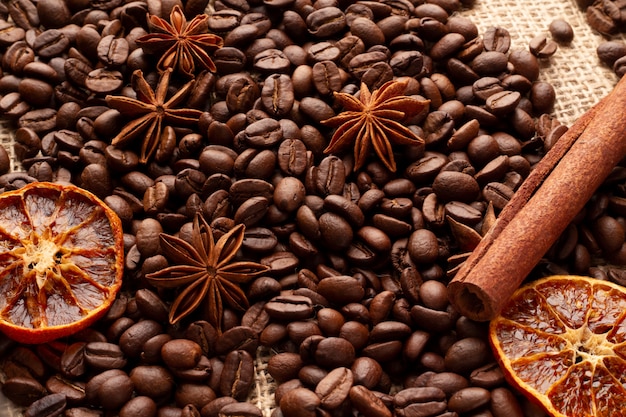 A table covered with coffee beans with cinnamon, anise stars and dried orange. 