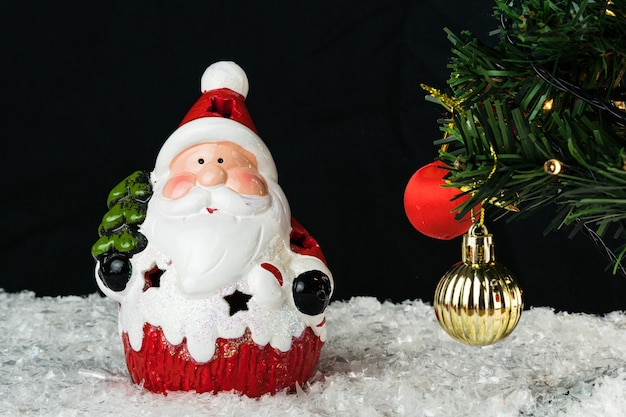 Table covered with snowflakes with Christmas decorations. Santa Claus, Christmas tree with red, gold balls and lights. Selective focus.