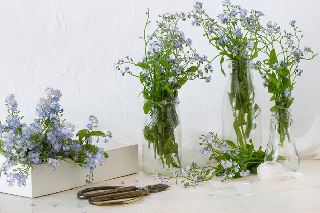 Photo on the table, forget me not in glass vases, forget me nots in a box, scissors and ribbon 