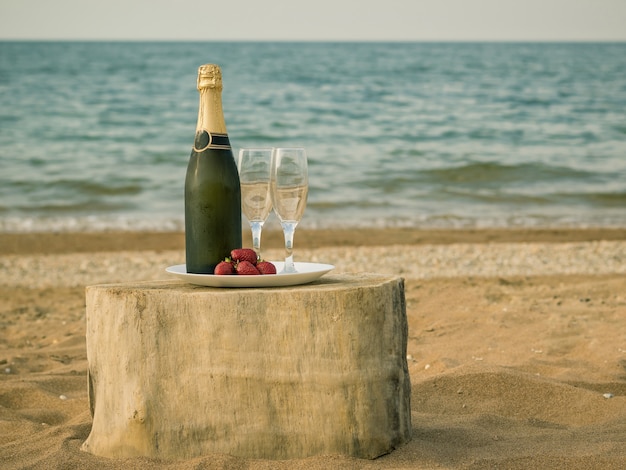 Table from a piece of wood with a bottle of champagne and strawberries by the sea.