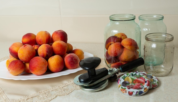 On the table is a dish with peaches jars for home canning lids for jars and a key for canning