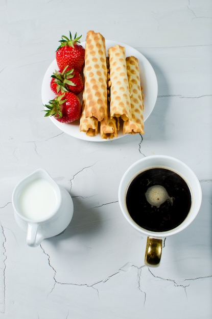 On the table is hot coffee, cream and sweet dessert with fresh strawberries