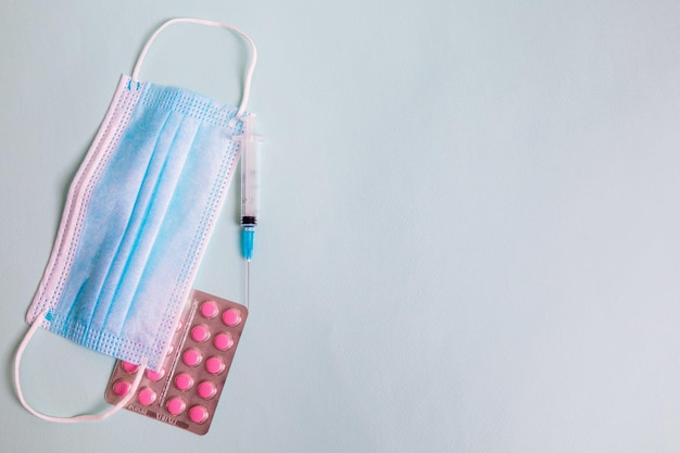 On the table is a medical mask with a syringe and medicine for coronavirus