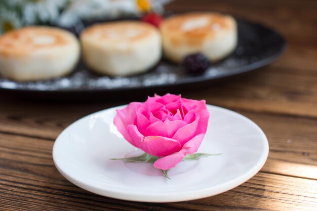 table setting with a rose on a saucer a plate with cheesecakes in the background