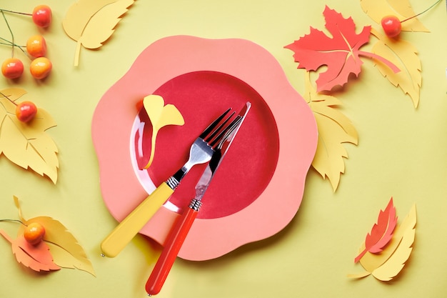 Table setup for Autumn celebration. Bright plastic plate on yellow paper with paper Autumn leaves