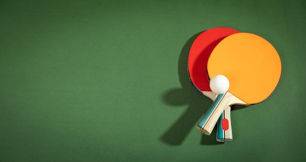 Table tennis rackets and a white plastic ball on the green background