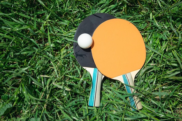 Table tennis rackets and a white plastic ball on the green grass background