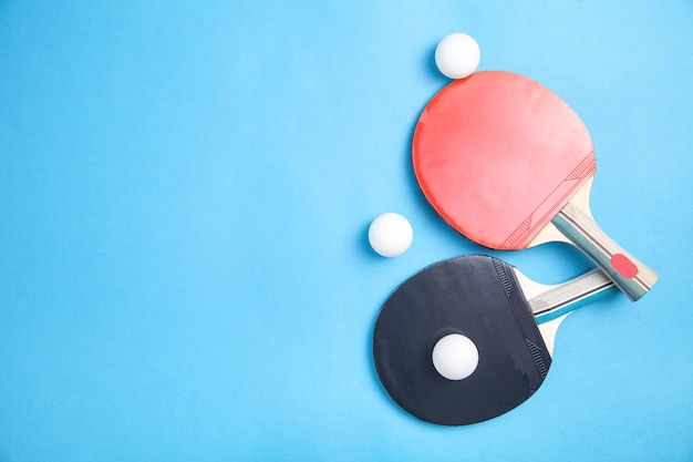 Table tennis rackets and a white plastic balls on blue, flat lay