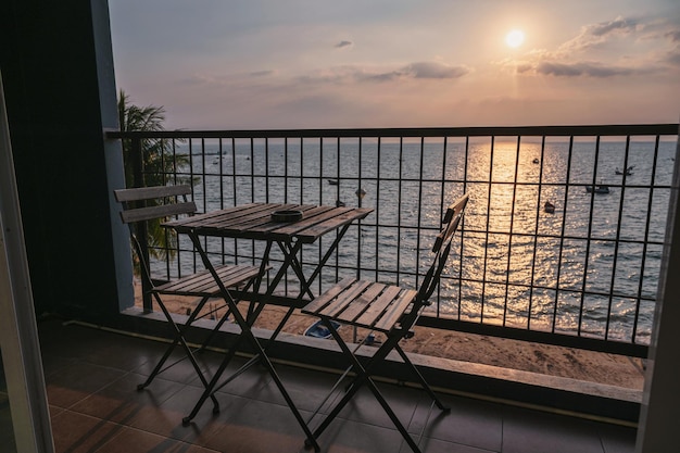 Table with chairs on terrace and sunset over sea