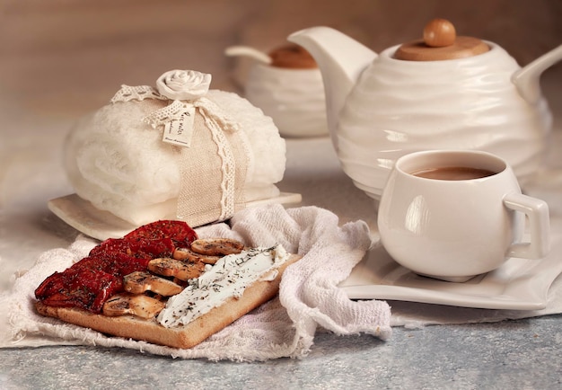 A table with a cup of tea and a sandwich with cheese and sauces.