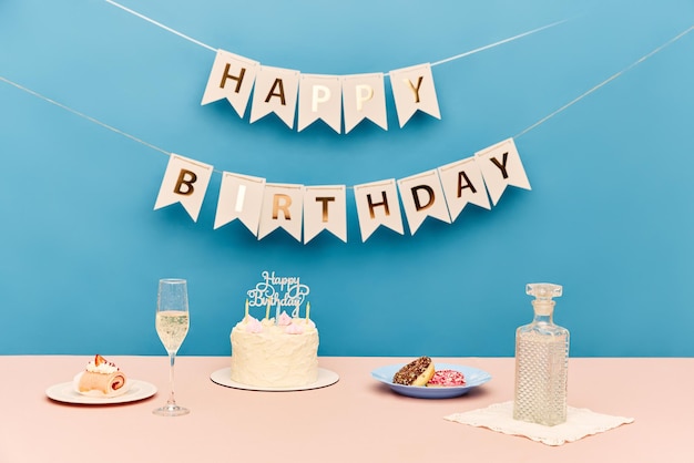 Table with delicious cake champagne and sweets against blue background with happy birthday letters