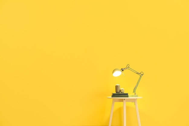 Table with glowing lamp near color wall in room