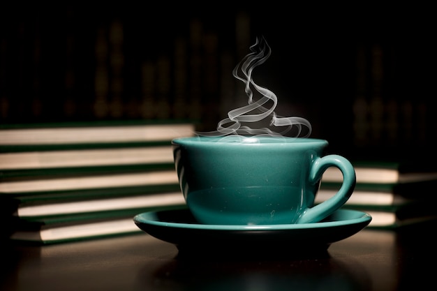 Table with green cup of hoy coffee with books black background space for text