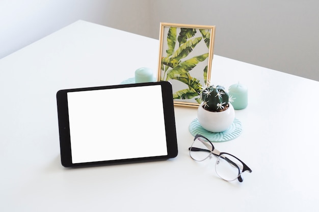 Table with tablet near photo frame and eyeglasses